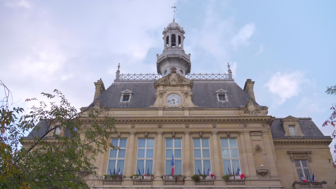 Un'inquadratura media e dal basso della sezione superiore dell'Hôtel de Ville di Asnières-sur-Seine, che evidenzia il suo orologio, la torre e la dettagliata architettura del XIX secolo sotto una chiara luce diurna.