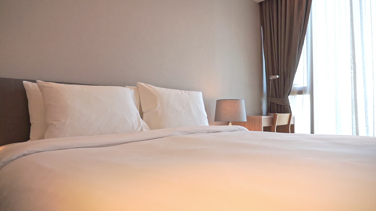 침대 옆 램프의 따뜻한 빛이 침대보를 비추는 침대의 발에서 머리까지