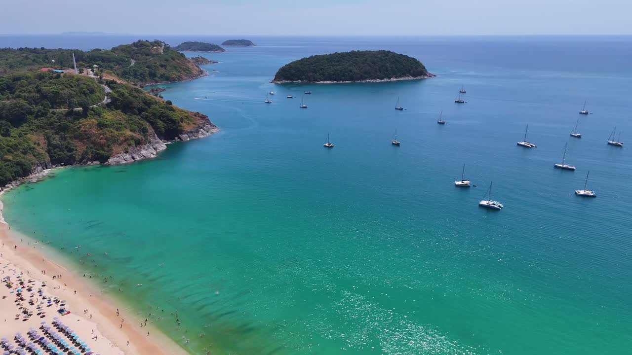 Imagens de drone capturam a Praia de Nai Harn em Phuket, Tailândia, exibindo águas azul-turquesa, barcos ancorados e uma costa vibrante.