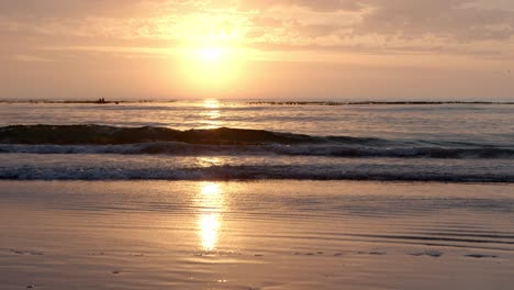 golden sunrise reflects on the wet beach as waves break and wash onto shore gently