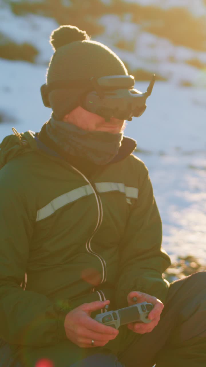 A focused individual wearing a green jacket and goggles operates a remote control in a snowy landscape, showcasing a serene yet engaging moment in a captivating outdoor environment