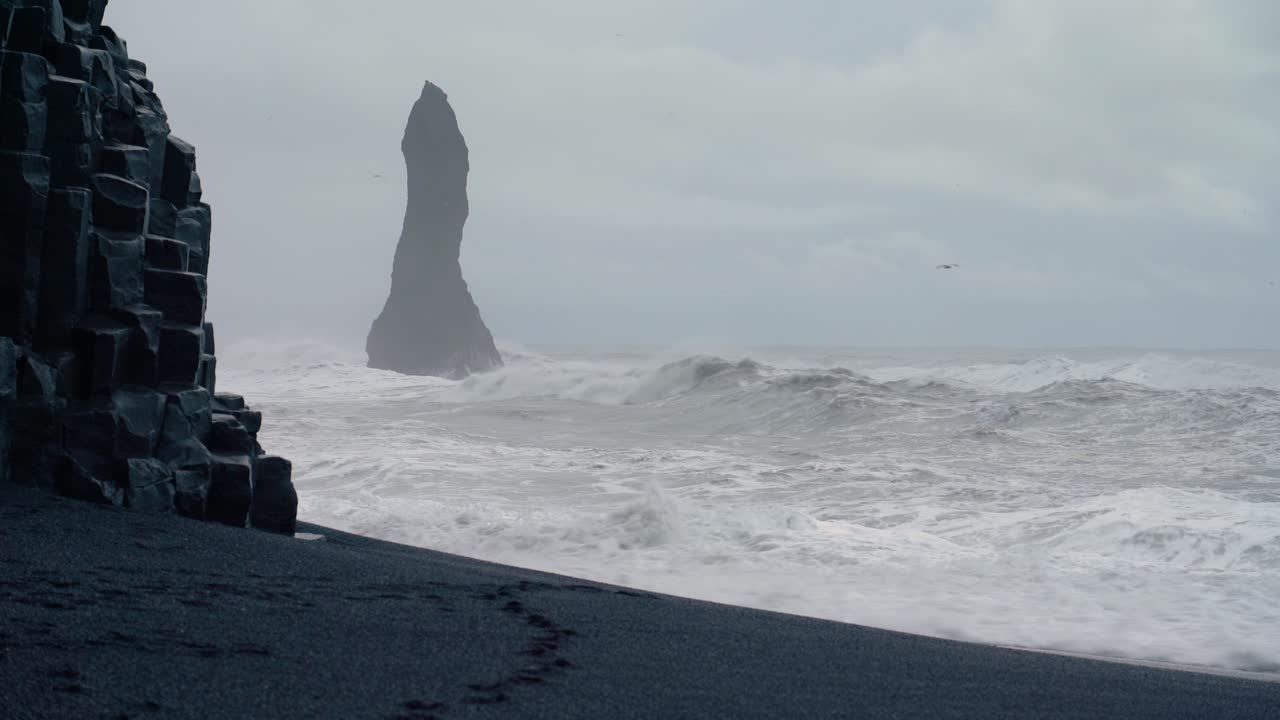 olas de zapatillas extremadamente peligrosas en la playa de arena negra de reynisfjara en islandia con una pila de basalto en el fondo brumoso