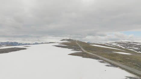 Semi-snow-covered-Storhovd-mountain-in-Norway-on-cloudy-day,-distant-telephone-mast