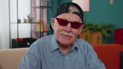 Stylish-grandpa-in-marijuana-cap-hat,-wearing-red-sunglasses,-looking-at-camera-with-charming-smile