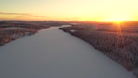 aerial view of sunset over snowy frozen lake in deep forest with hills and mountains