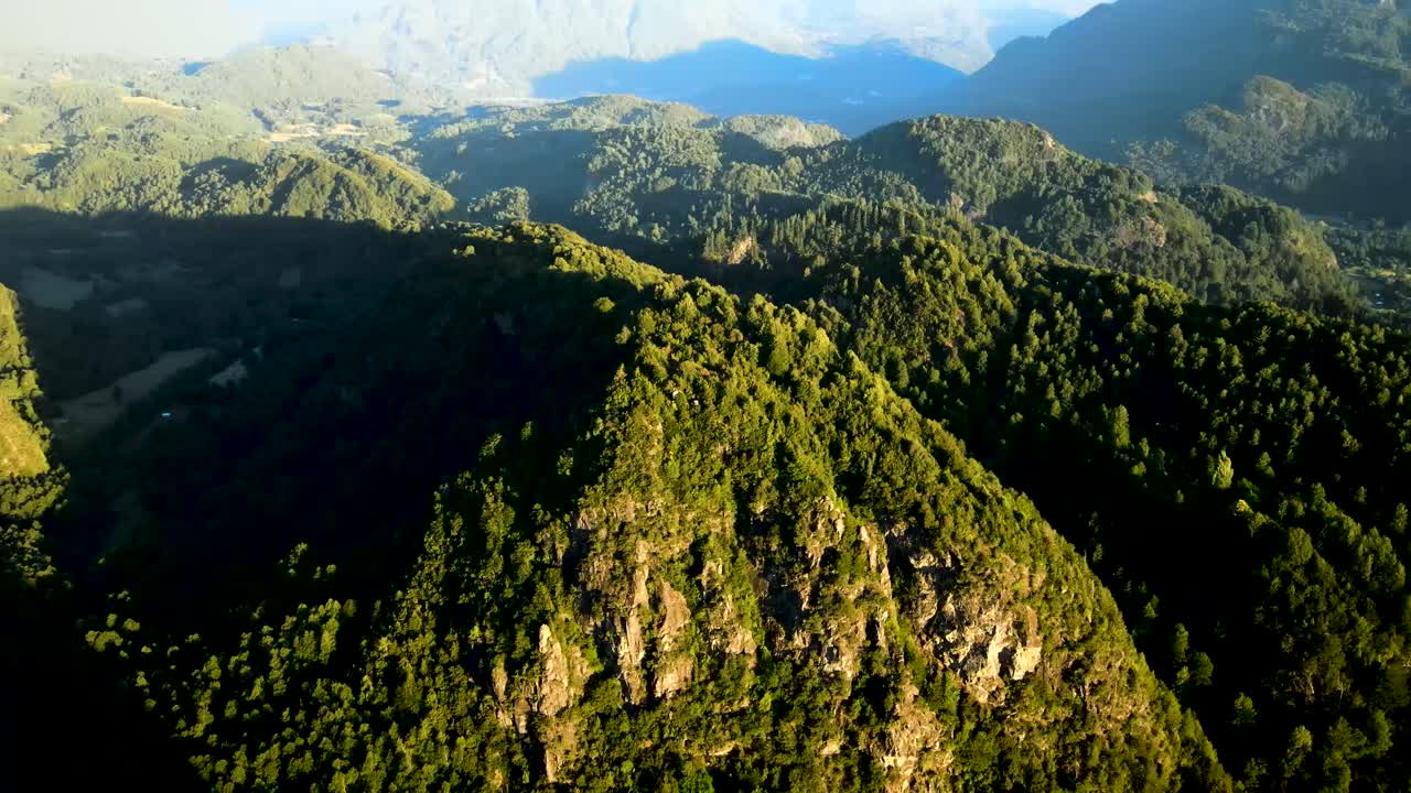 panorámica aérea a la derecha de las montañas andinas cubiertas de densos bosques verdes a la hora dorada en el mirador de el león, chile