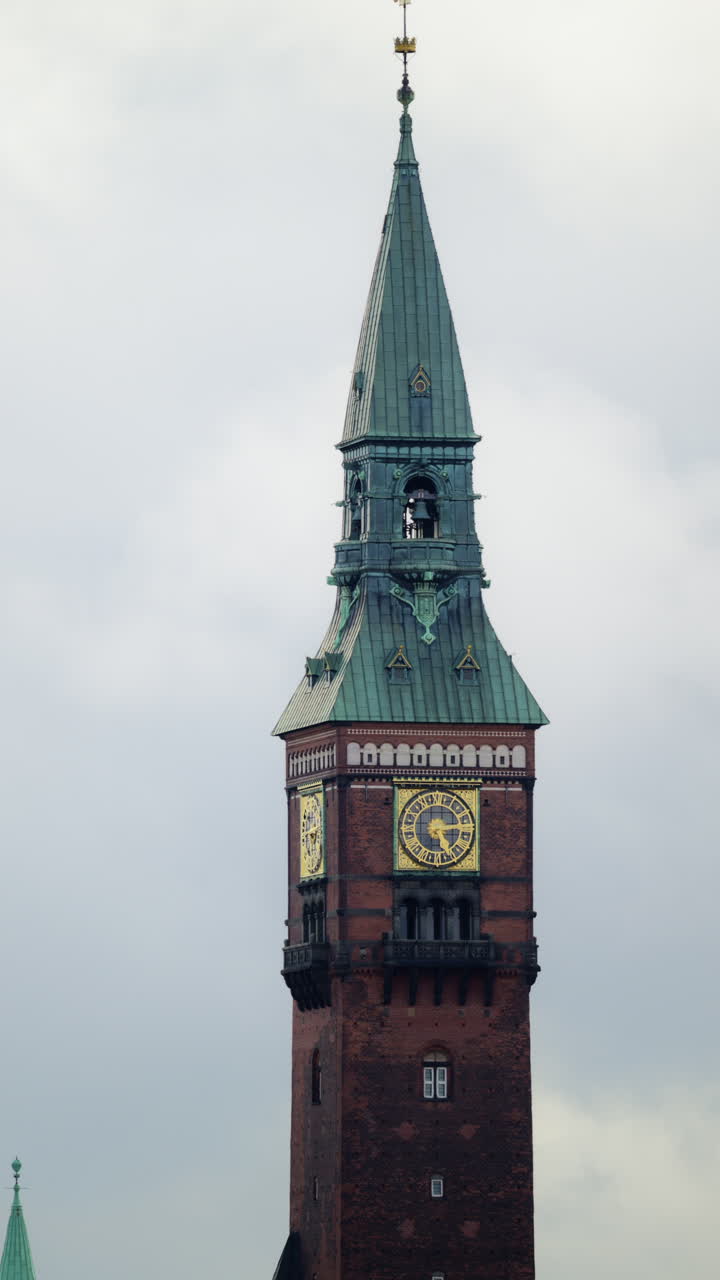 Ornate clock tower of Copenhagen City Hall reaching into a gray sky over rooftops