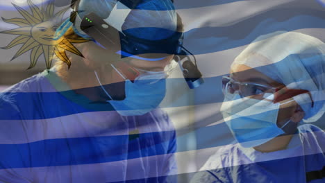 animation of uruguay flag against diverse male and female surgeons performing operation at hospital