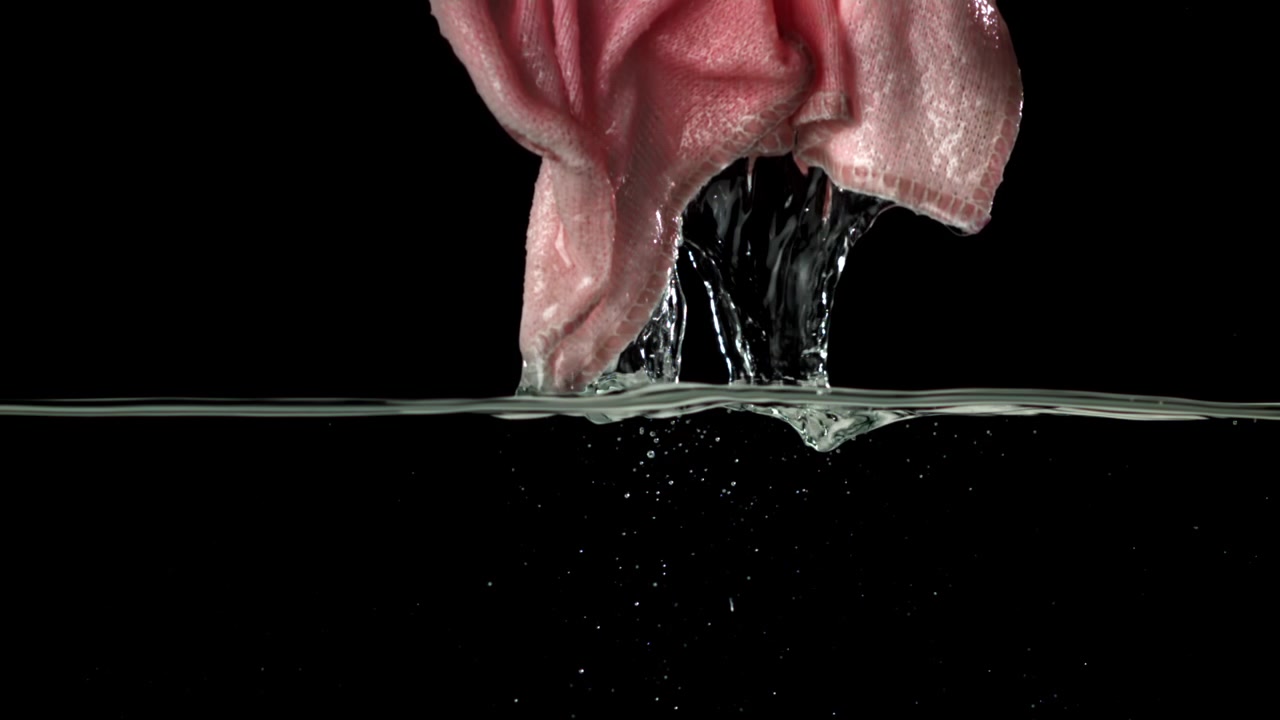 Primo piano di una mano che strizza l'acqua da un panno rosa bagnato