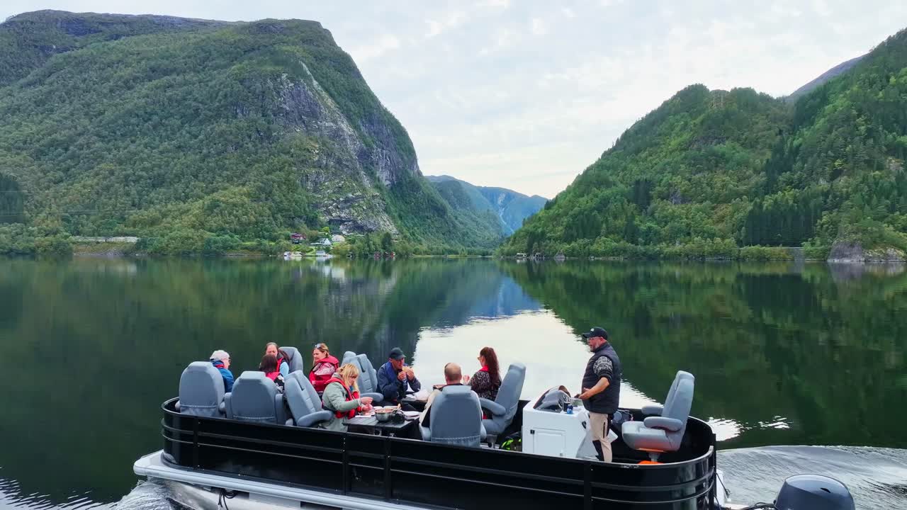 Drone follows pontoon cruising through Bolstadfjord, revealing lush valley and mountains in the background