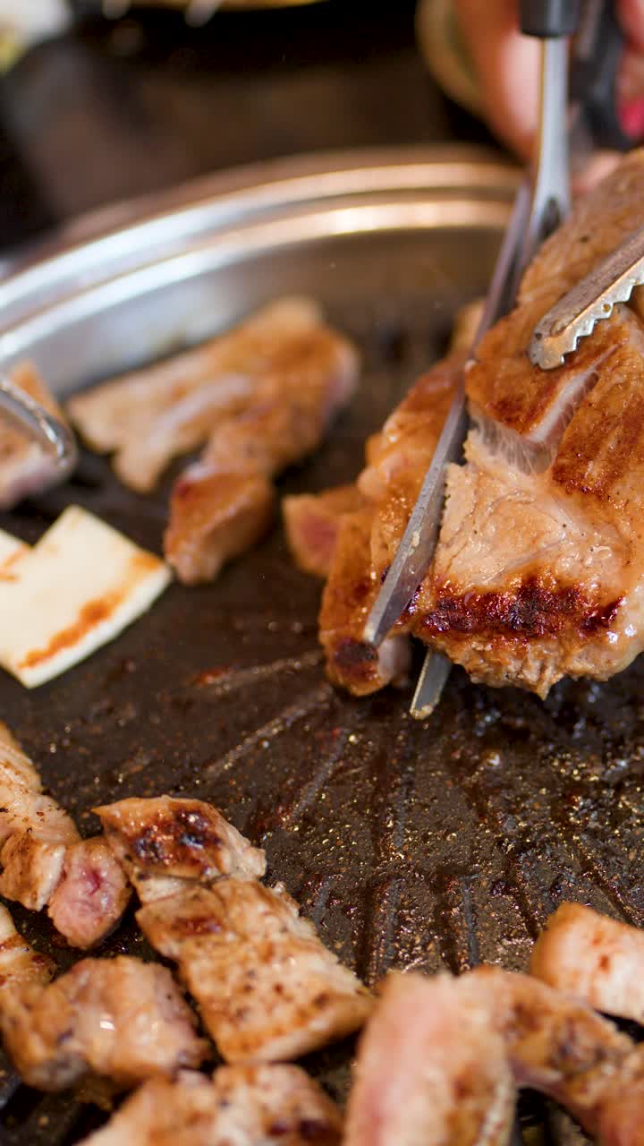 Perut babi yang dipanggang dan diiris dengan penjepit di atas barbekyu Korea meja, pencahayaan dalam ruangan yang hangat