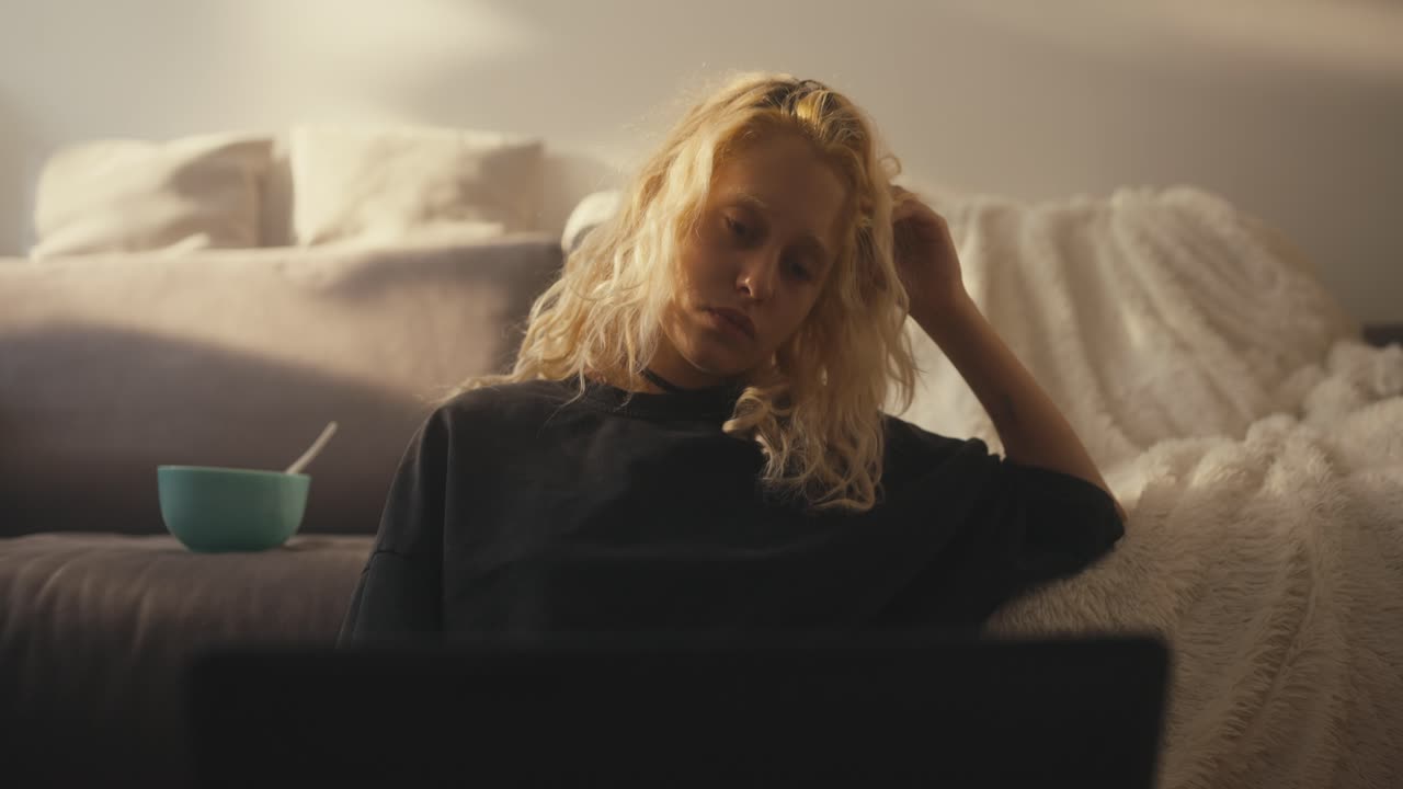 Sad blonde girl in a black T-shirt closes her laptop when loved ones call out to her late at night