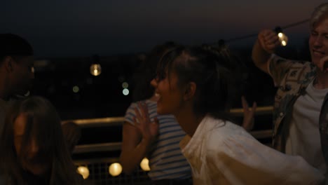 group of friends dancing at the party in top of the roof at night.