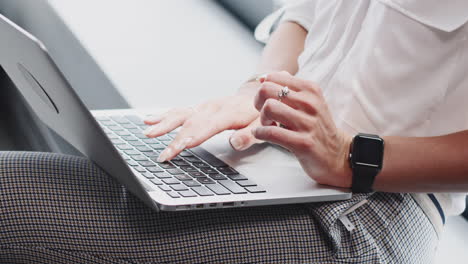 White-woman-with-long-manicured-fingernails-using-a-laptop-computer-on-her-knee,-close-up-of-hands