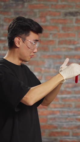 asian scientist tastes homemade red alcohol liquid from test tube having fun with african-american friend in spacious pharmaceutical laboratory