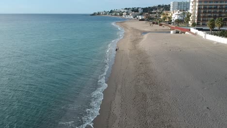 aerial views over a beach with gentle waves and people walking along the shore calmly