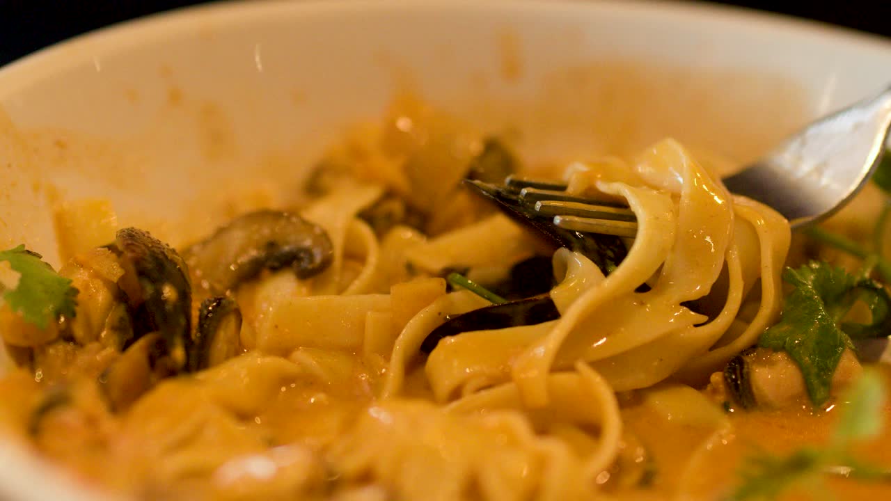 Close-up of fork twirling creamy seafood pasta with mussels in warm, softly lit setting