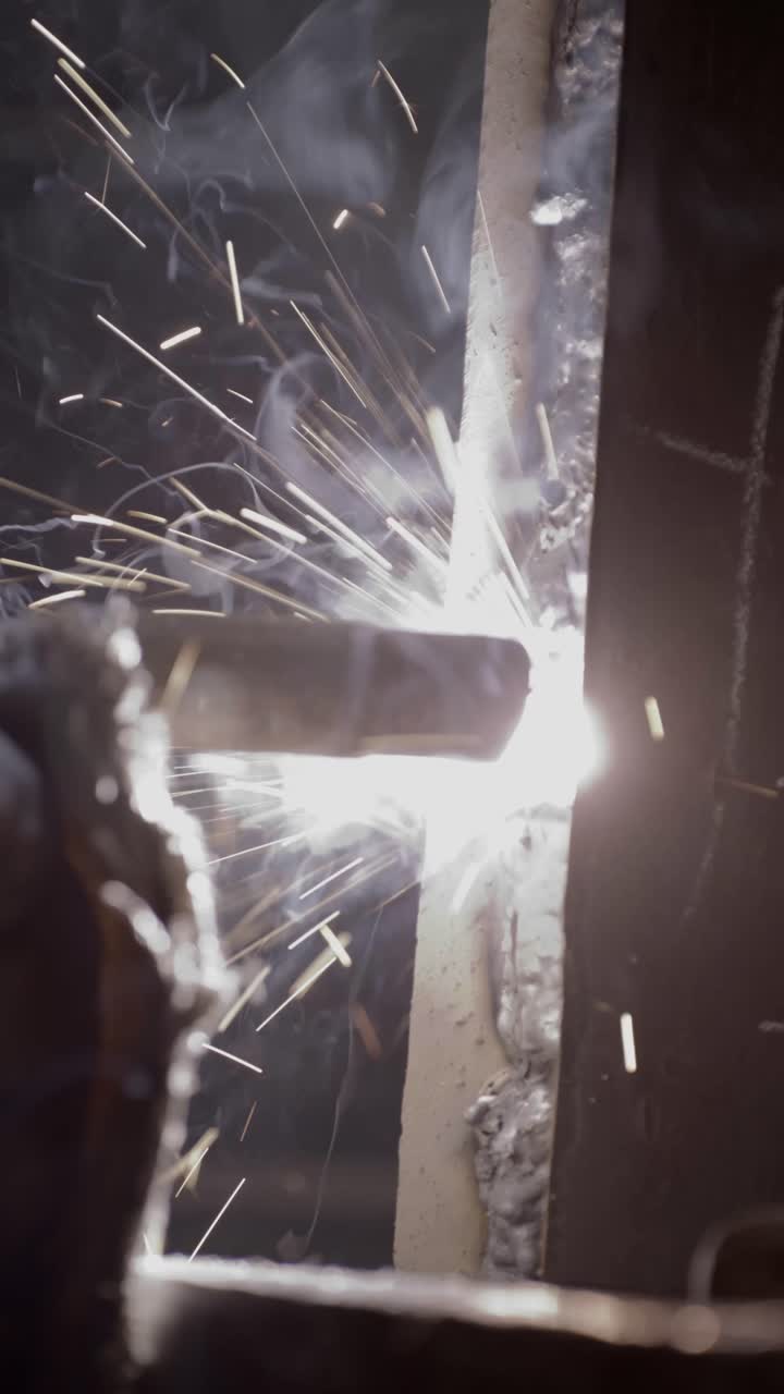 Vertical extreme close up footage of welding with bright sparks flying during metal fabrication. Industrial manufacturing scene showing skilled labor, heat, and precision work, ideal for industry, con