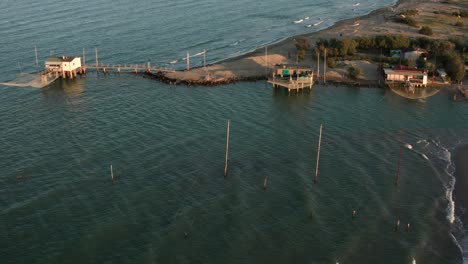 Aerial-shot-of-the-valleys-near-Ravenna-where-the-river-flows-into-the-sea-with-the-typical-fishermen's-huts-at-sunset