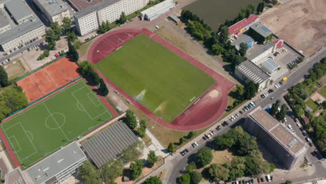 Backwards-reveal-of-sports-centrum.-Aerial-view-of-area-for-doing-various-sports,-football-pitch,-tennis-courts-and-athletic-sports-field.-Berlin,-Germany