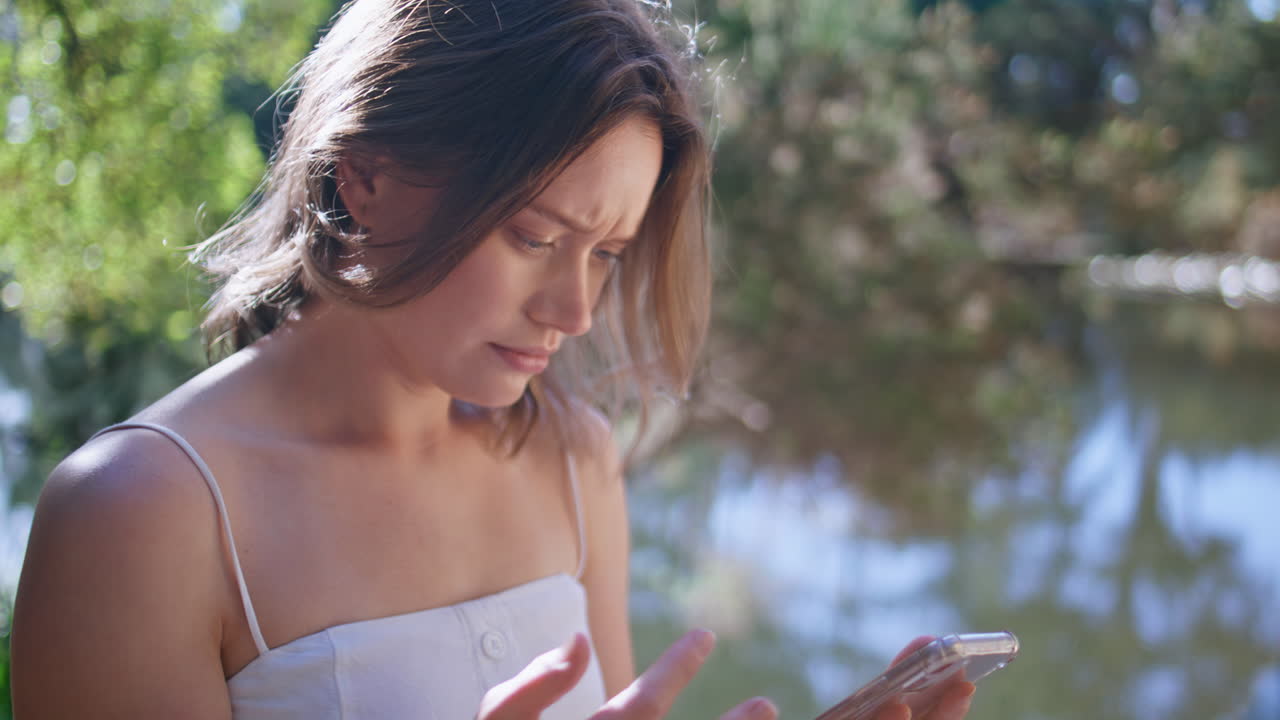 Worried woman using mobile phone confused broken device in sunny park closeup