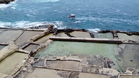 Vista-Aérea-De-Un-Bote-Pequeño-Cerca-De-Salinas-En-Malta