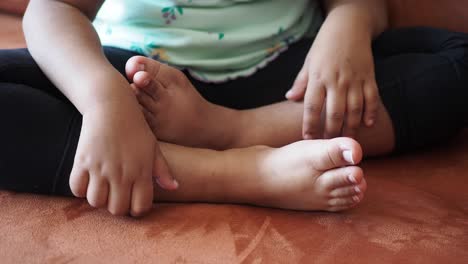 una niña pequeña está sentada con los pies cruzados, y se ha pintado los dedos de los pies. lleva leggings verdes y negros y tiene las manos en las piernas. la niña está sonriendo.