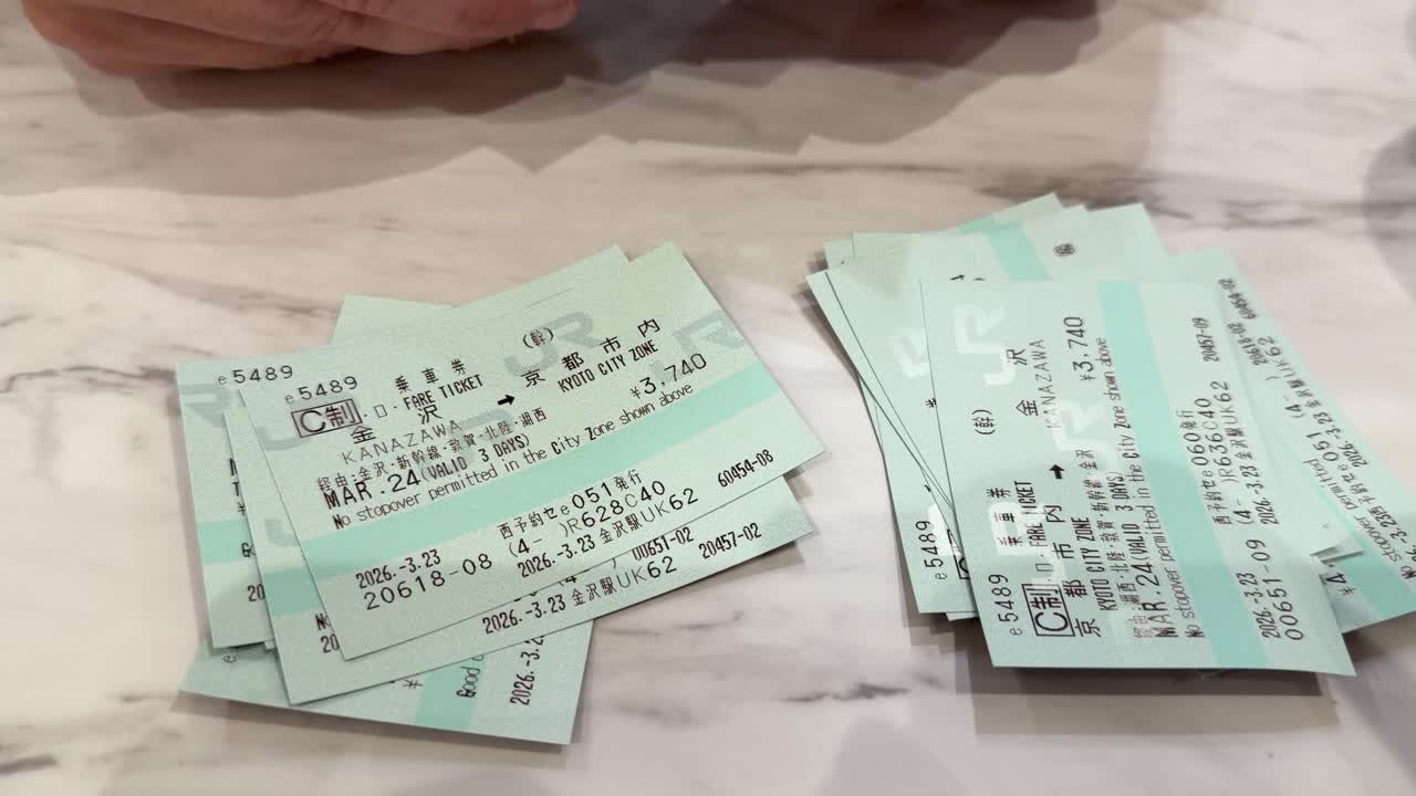 Close-up shot of hands organizing multiple green paper train tickets on a white marble surface