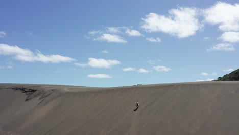 Man-struggles-to-walk-up-long-foredune-on-Bethells-beach-in-New-Zealand