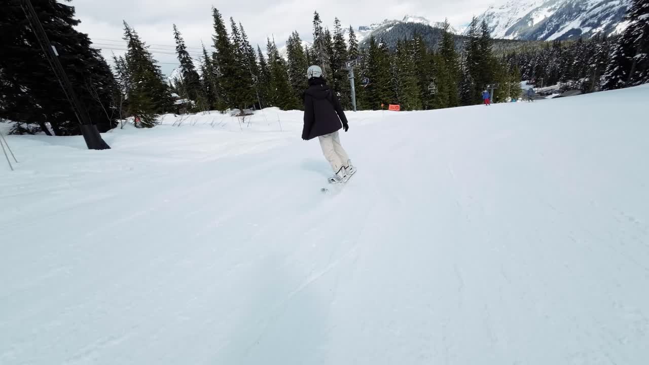 siguiendo a una mujer adulta brasileña alta vestida con equipo de nieve blanco y negro haciendo snowboard en cámara lenta por un sendero de la estación de esquí rodeado de pinos en snoqualmie washington, estados unidos