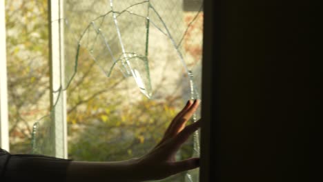 Hand-moves-across-broken-glass-window