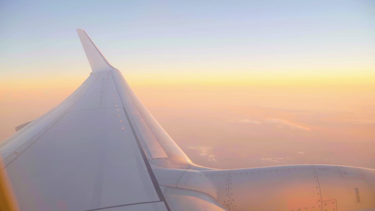 vista de la ventana de un ala de avión con una suave puesta de sol de color pastel en las nubes