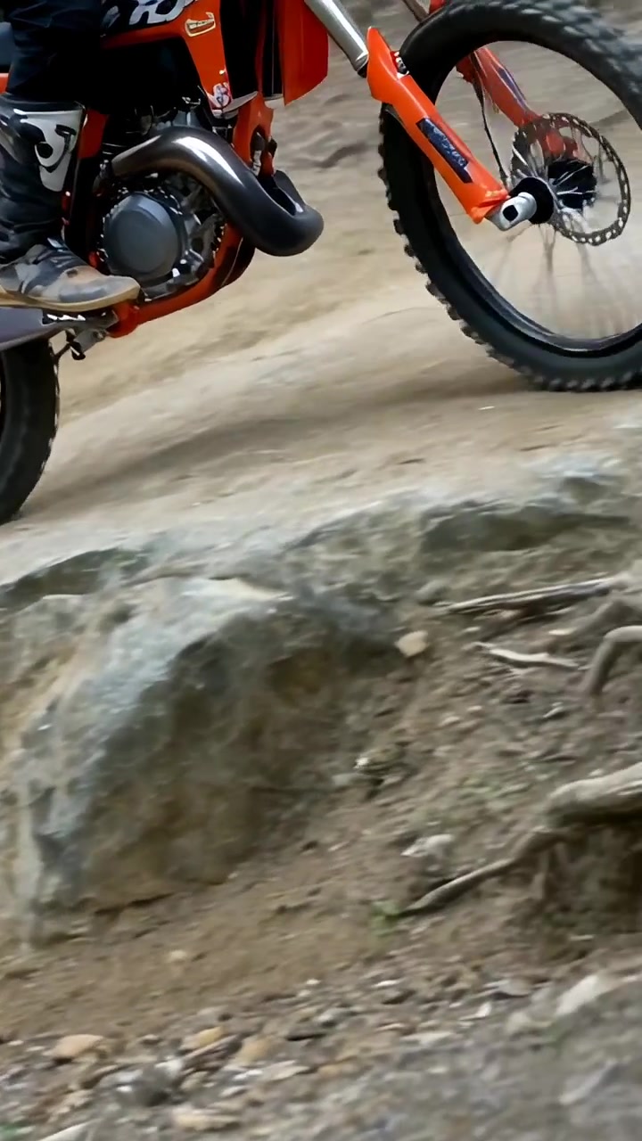 Vídeo vertical: Ciclista em bicicleta laranja se aproximando de rocha, acelerando, levantando a roda dianteira, superando a rocha, botas.