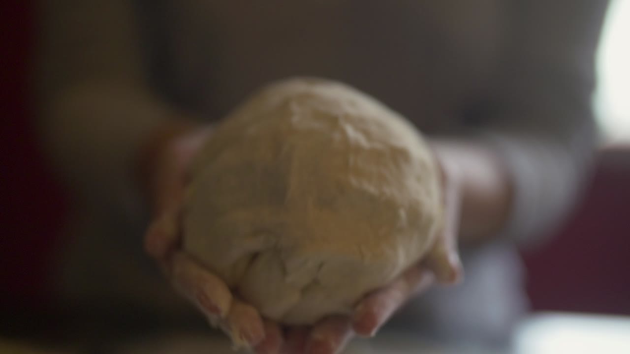 Woman's hand show rounded ball of pizza dough to camera