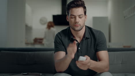 Handsome-man-switching-remote-control-on-sofa-at-open-kitchen.