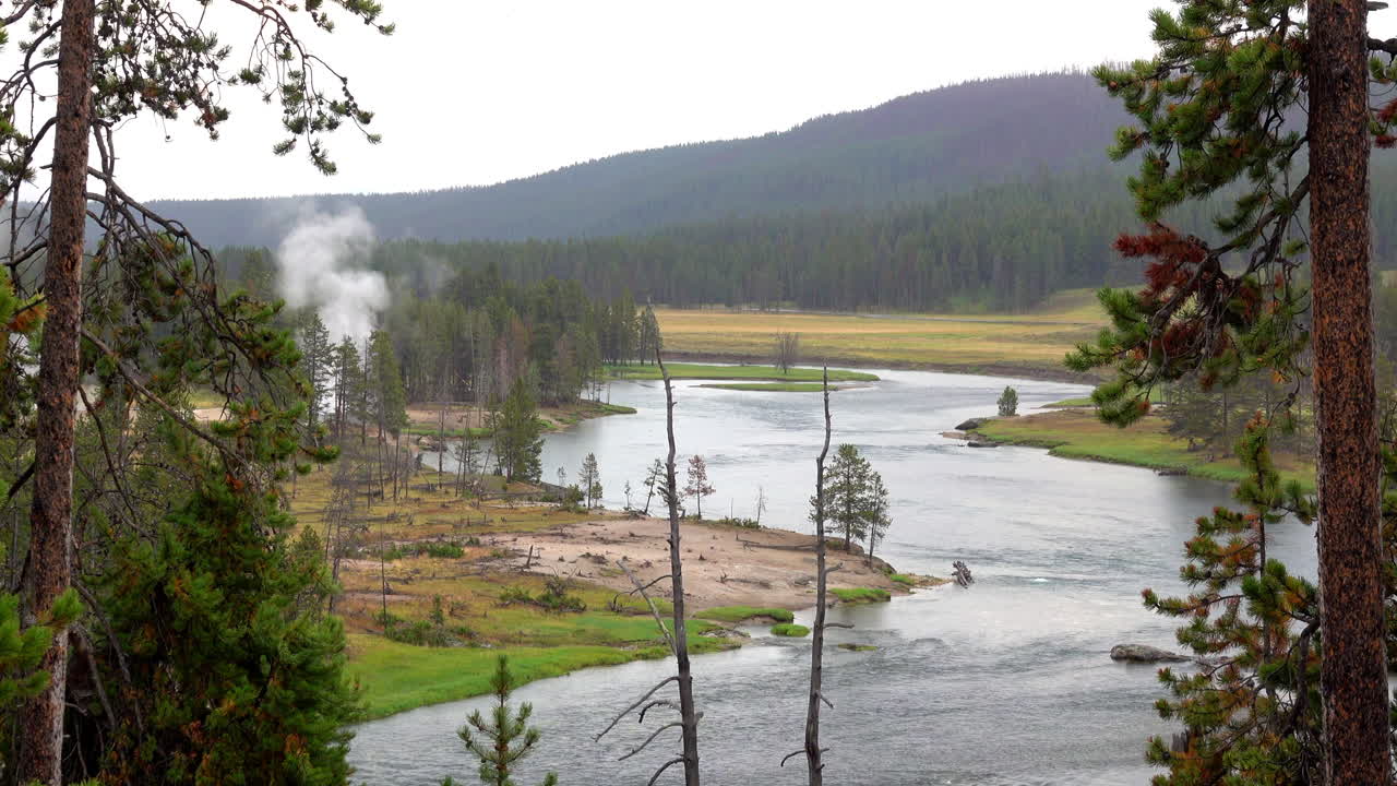 Landskap i Yellowstone nationalpark med Yellowstonefloden, berg och geotermisk aktivitet.