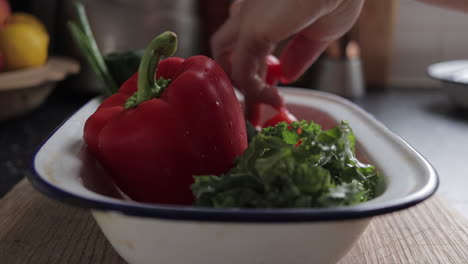 mujer colocando tomates en una fuente para hornear esmaltada con pimiento rojo y col rizada en una tabla de cortar de madera