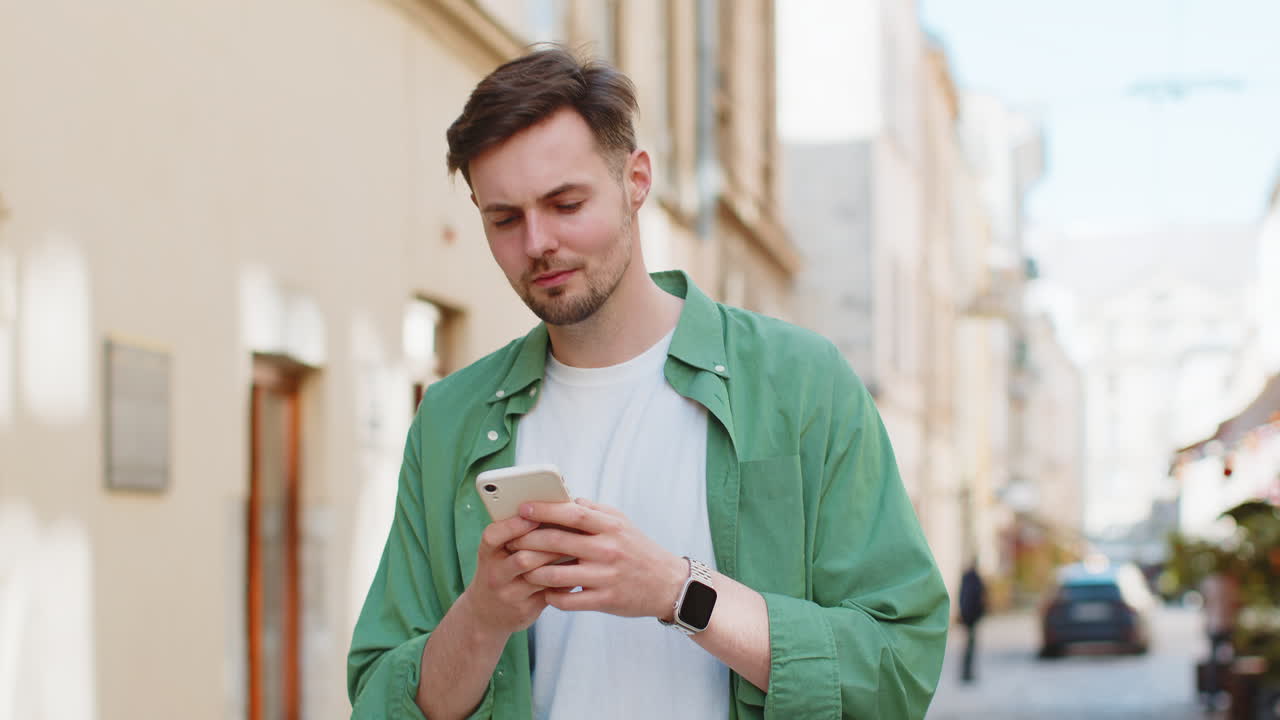 Uomo felice che usa lo smartphone per digitare messaggi, scrivere su app di social media ed e-mail in una strada cittadina.