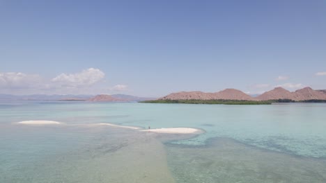 一名男子站在白沙岛上,周围是海底浅水,后面是科莫多岛 - - 空中轨道