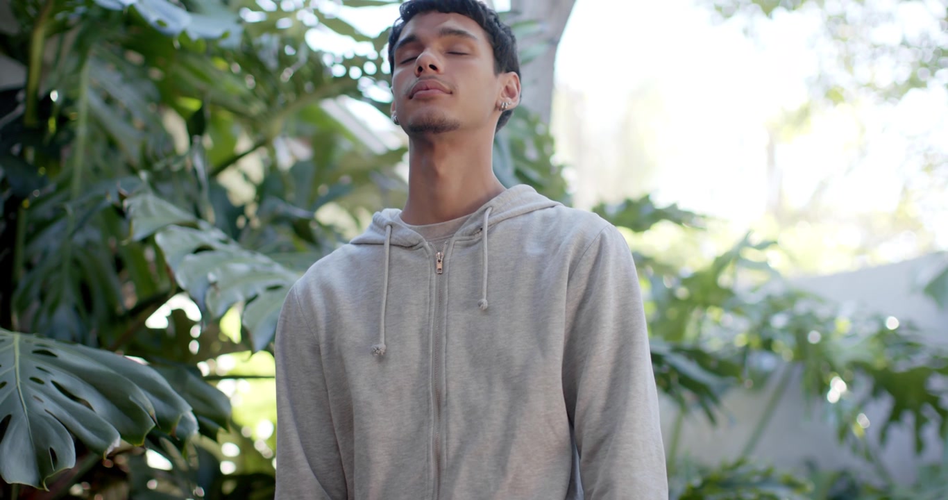 Uomo afroamericano con felpa grigia con cappuccio in un cortile, mentre la telecamera rivela il suo volto, si inclina all'indietro e respira