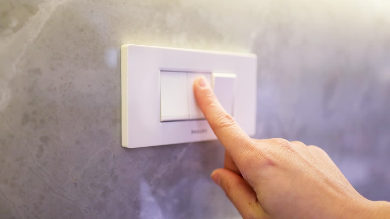 A hand presses a white light switch on a marble wall, changing lighting to purple