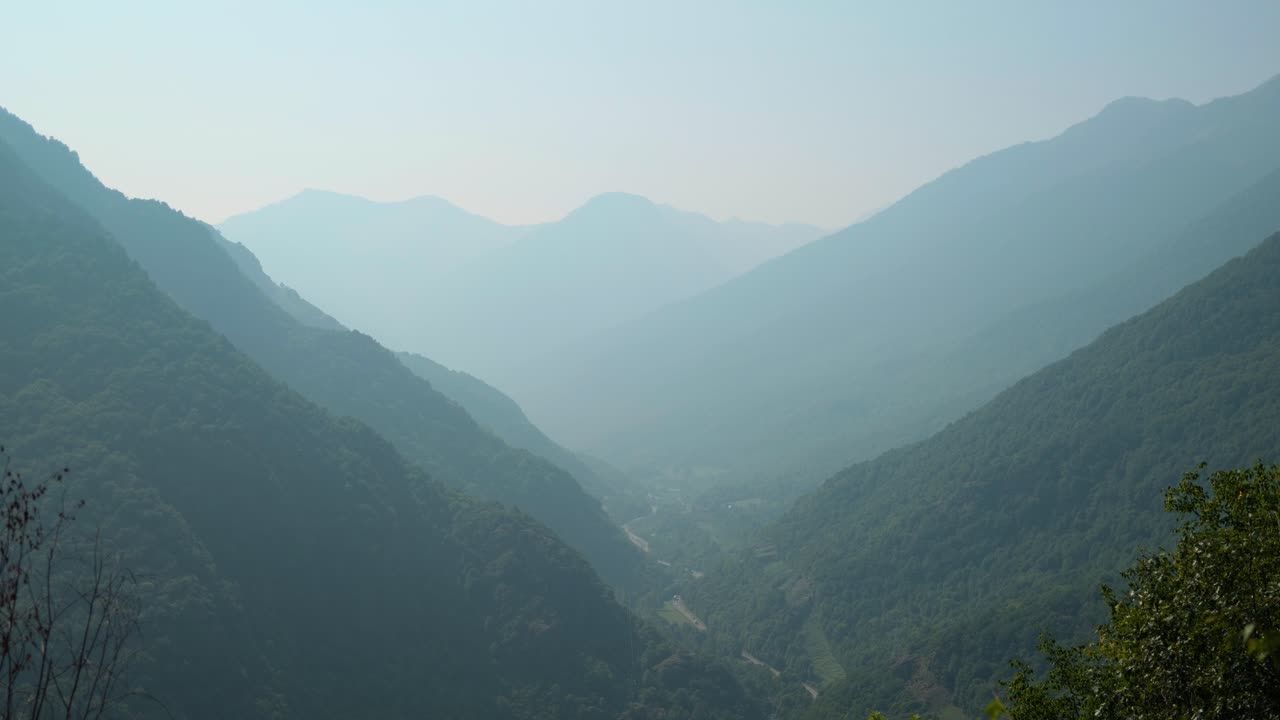 Misty mountains and lush valleys stretch into the distance under a soft, hazy sky