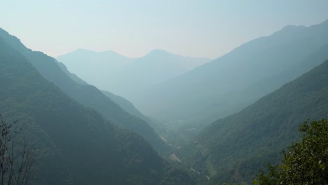 misty mountains and lush valleys stretch into the distance under a soft, hazy sky