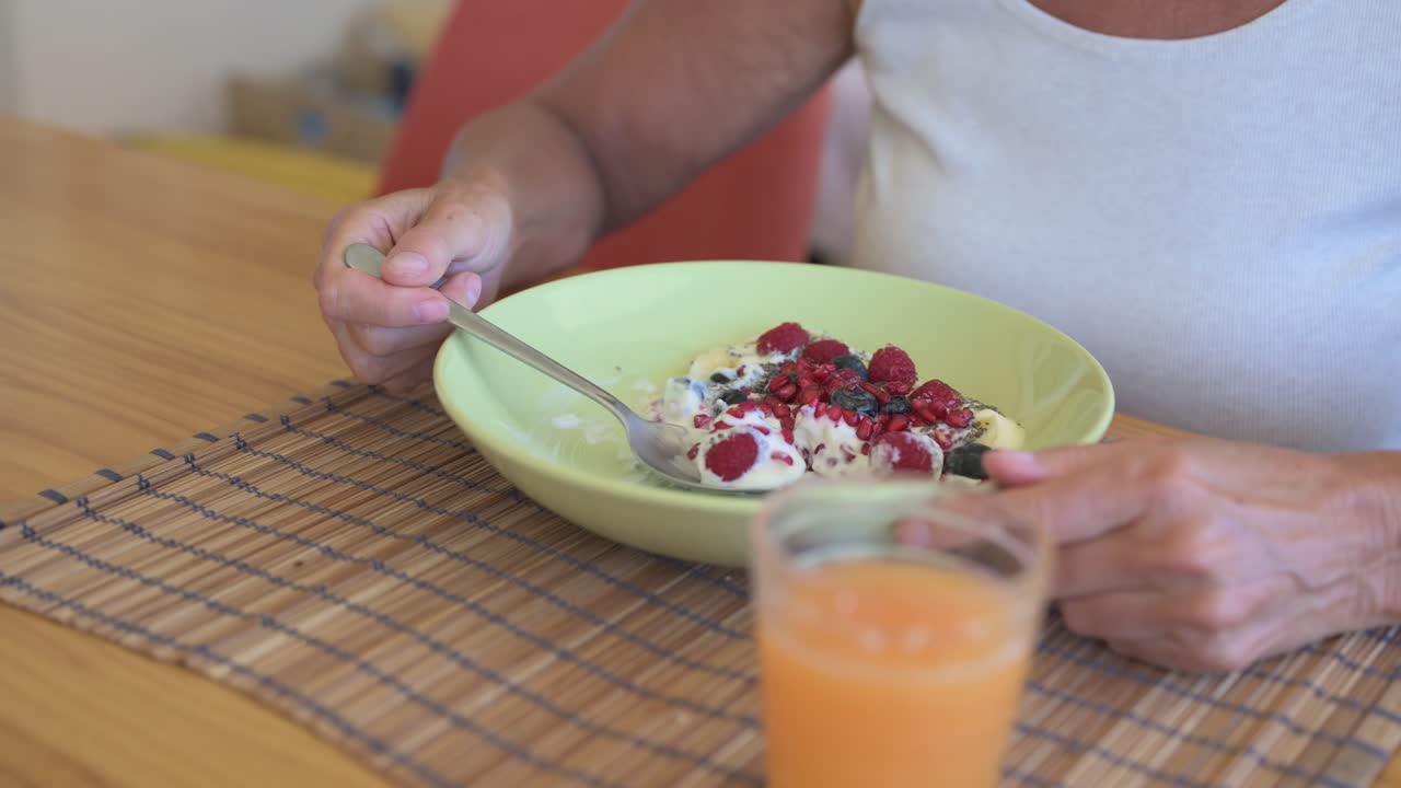 Close-up of female eating healthy homemade yoghurt for breakfast with orange juice glass on table