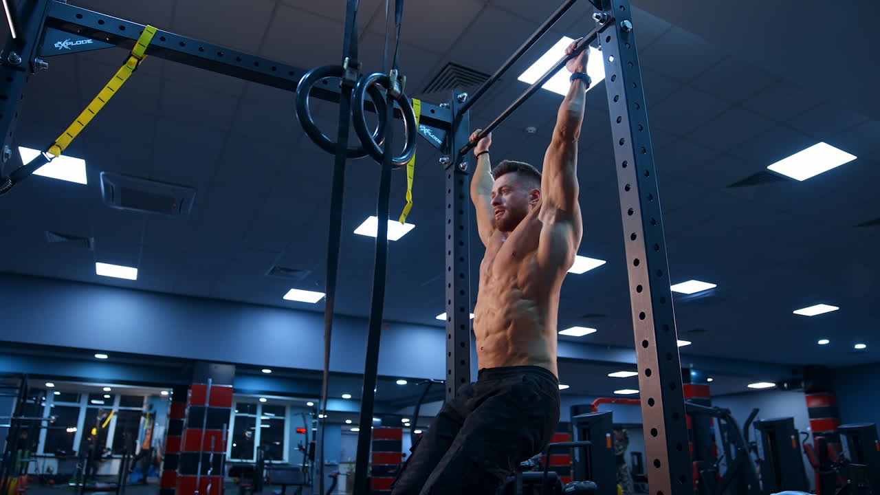 Bodybuilder exercising on horizontal bar. Shirtless man pulling up on horizontal bar in gym