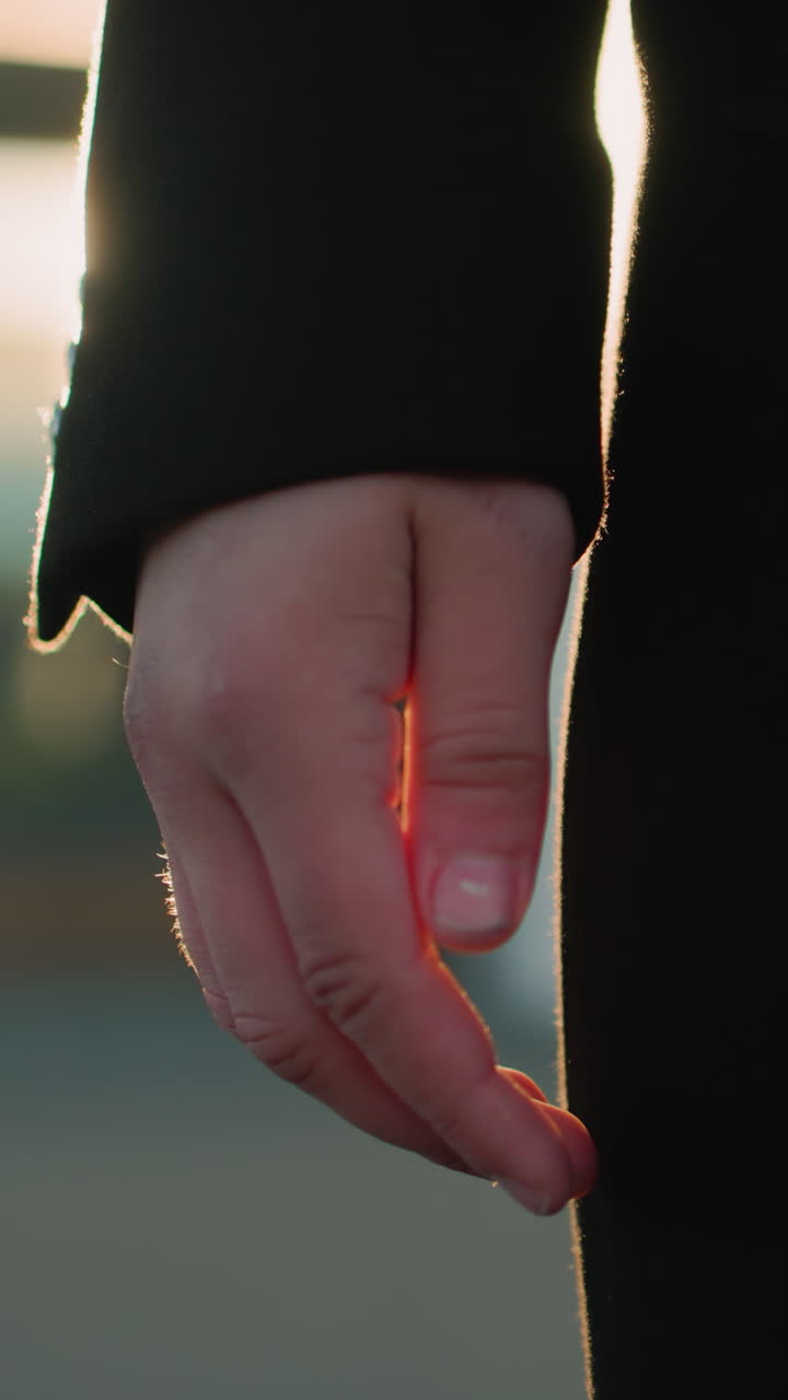 황금색 빛에 부드럽게 빛나는 검은색 수갑을 입은 손의 클로즈업, 편안하지만 의도적인 자세를 보여주는, 따뜻하고 흐릿한 배경은 반사 빛으로 도시 환경을 강조합니다.