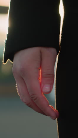 primer plano de la mano en la manga negra suavemente iluminada por la luz del sol dorada, mostrando una postura relajada pero intencional, el fondo cálido y borroso destaca el entorno urbano con luz reflectante