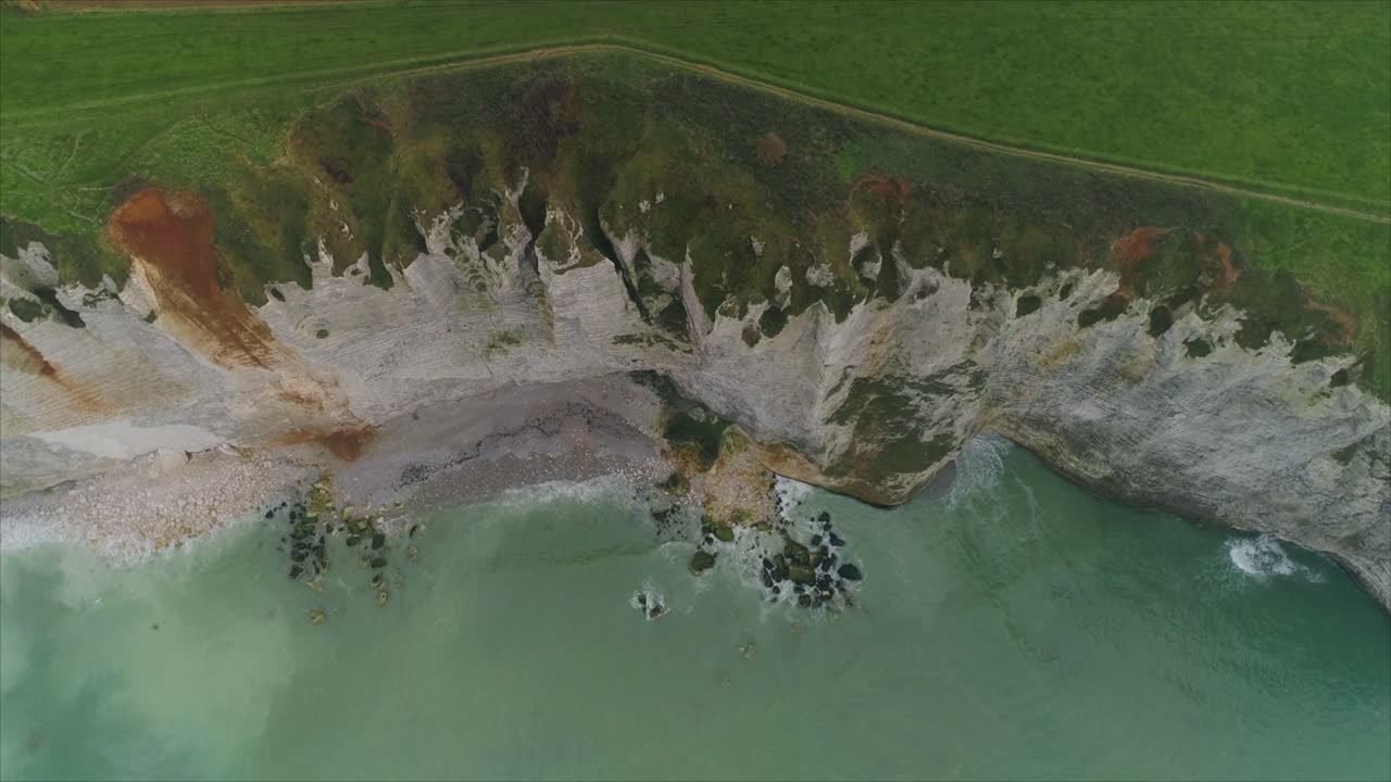 Vista aerea con drone delle bianche scogliere di gesso di Etretat che incontrano il mare turchese, con una costa frastagliata e onde sottostanti, sotto la luce soffusa del giorno in Normandia, Francia.