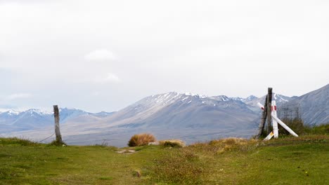 fence posts on green meadow on windy day in new zealand with stunning mountains in background