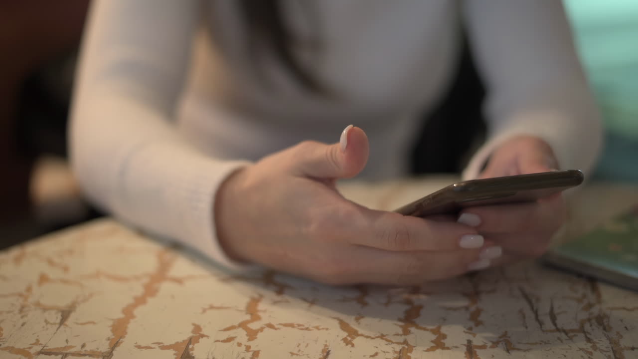 Primo piano di una donna che gesticola mentre tiene in mano il telefono a un tavolo in un bar